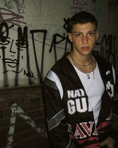 a young man standing next to a wall covered in graffiti