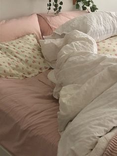 an unmade bed with pink and white sheets, pillows and plants on the headboard