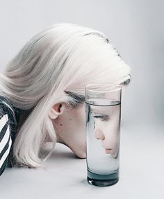 a woman with her head in a glass next to a drinking glass that is half empty