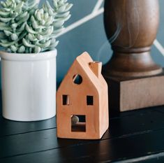 a small wooden house next to a potted plant on a black table with blue wallpaper