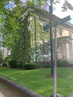 a street sign in front of a large white building with ivy growing up the side of it