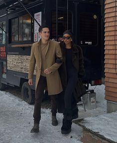 a man and woman standing in front of a food truck on the snow covered ground