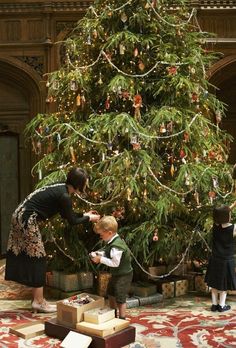 two children and an adult standing in front of a christmas tree with presents on it