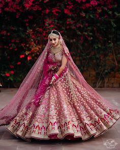 a woman in a pink and gold bridal gown standing on the ground with flowers behind her