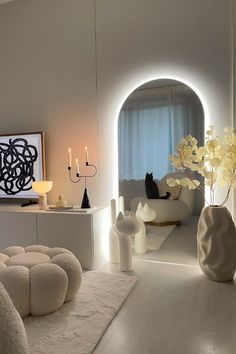 a living room filled with white furniture and candles on top of the tables in front of a window