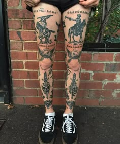 a person with tattoos on their legs standing in front of a brick wall