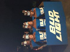 six people wearing blue and brown shirts in a cardboard box with bud light on it