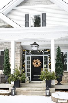 a white house decorated for christmas with wreaths and potted trees on the front porch