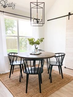 a dining room table with four chairs and a vase on top of it in front of a window