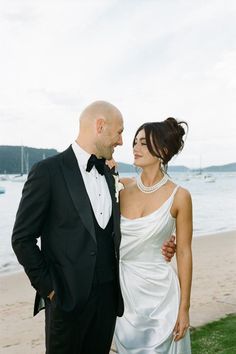 a man in a tuxedo and a woman in a wedding dress standing on the beach