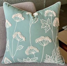 a blue pillow with white flowers on it sitting on a gray couch next to a table