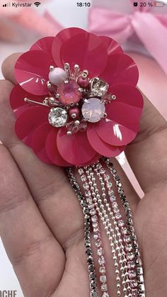 a hand holding a pink flower brooch in it's left hand with pearls and crystals on it