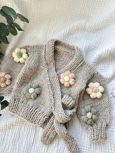 a knitted sweater with flowers on it laying on top of a white blanket next to a potted plant