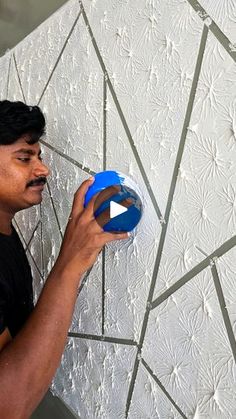 a man holding a blue object in front of a white wall with geometric designs on it