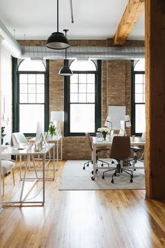 an office with wooden floors and brick walls, along with white chairs and desks