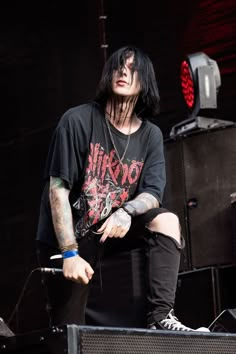 a man with black hair and piercings sitting on a stage