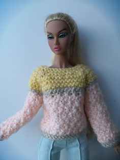 a doll with blonde hair wearing a pink and yellow knitted sweater on top of it's head