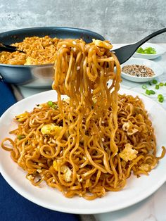 noodles being lifted from a plate by tongs on a table with other dishes in the background