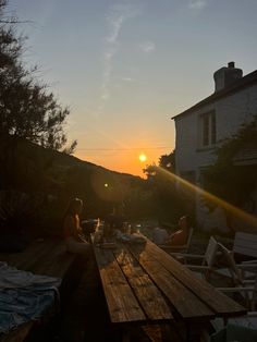 the sun is setting over some people sitting at a picnic table in front of a house