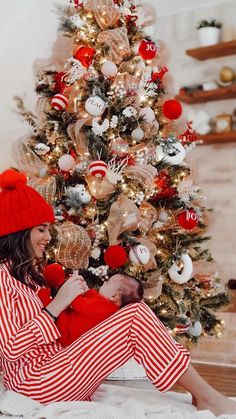 a woman sitting on the floor in front of a christmas tree wearing red and white pajamas