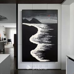 a black and white painting hanging on the wall in a living room next to a kitchen