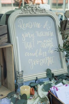 a sign with writing on it sitting next to some flowers and other items in front of a window