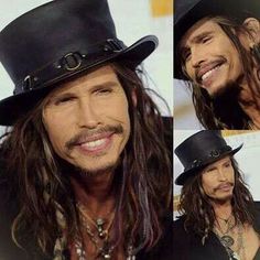 a man with long hair wearing a black top hat and smiling at the camera,