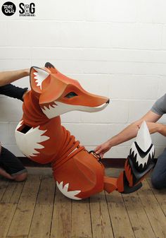 two men are sitting on the floor and one is holding a paper mache that looks like a fox