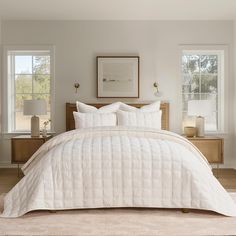 a bed with white comforter and pillows in a bedroom next to two lamps on either side of the bed