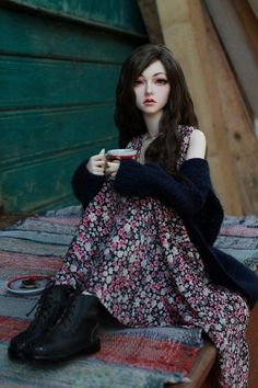 a doll is sitting on the ground holding a cup