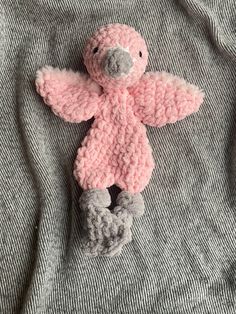 a crocheted pink teddy bear laying on top of a gray shirt