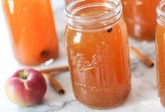 three jars filled with liquid sitting on top of a table next to apples and cinnamon sticks