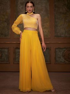 This is a two-piece Yellow Thread Flared Pant Set from the Suruchi Parakh collection. The one-shoulder yellow crop top in georgette is paired with matching flared pants. The top is padded and has a back hook opening. There is beautiful floral thread hand-embroidery with collar on the top. The yellow color with sequin, pleats and bishop sleeves enhances the graceful, flared pant set in georgette fabric. Haldi Dress, Haldi Outfits, Haldi Outfit, Raw Silk Lehenga, Yellow Lehenga, Green Lehenga, Yellow Crop Top, Floral Embroidered Top, Top And Pants Set