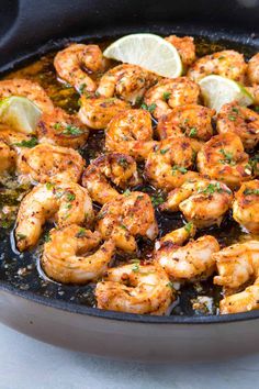 a skillet filled with shrimp and lemon wedges