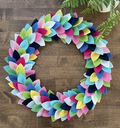 a wreath made out of colored paper sitting on top of a wooden table next to flowers