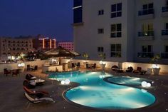 an outdoor swimming pool with lounge chairs and lights around it at night in the city