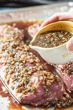 a person pouring sauce on top of some meat