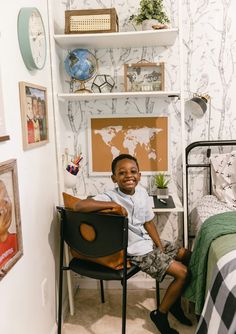 a young boy sitting in a chair next to a bed