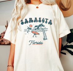 Sarasota Florida Beach Surfer Crewneck Sweatshirt, Unisex Womens Florida Pullover Gift The Comfort Colors C1717 100% Ring Spun Cotton T-Shirt is very appropriately-named. All colors are inspired by nature and have a perfect lived-in, weathered look. Shirts are sent through a unique dyeing process that makes them incredibly soft and long-lasting. Each piece is soft-washed 50 times before making its way to you! Stitched at the collar, armhole, sleeves and bottom hem for ultimate durability, you will notice the density and quality of this shirt, but won't mind living in it. COMFORT COLORS 1717 ADULT TEE 6.1 Oz/SqYd 100% Ring Spun Cotton Soft-washed garment-dyed fabric Double-needle collar Twill taped neck and shoulders Twill label Relaxed fit Double needle armhole, sleeve and bottom hems Tubu White Soft-washed Vacation Top, White Soft-washed Top For Vacation, Soft-washed White Vacation Top, Soft-washed Crew Neck Top For Vacation, Crew Neck Tops For Beach Loungewear, Leisure Crew Neck Tops For Beach Season, Leisure T-shirt With Letter Print For Beach Season, Casual Beach Season T-shirt, Cotton T-shirt For Beach Season Leisure