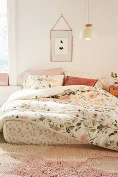 a bed with floral sheets and pillows in a white room next to a pink rug