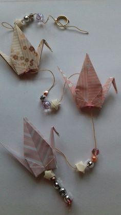 three origami cranes are hanging from strings on a white surface with beaded beads