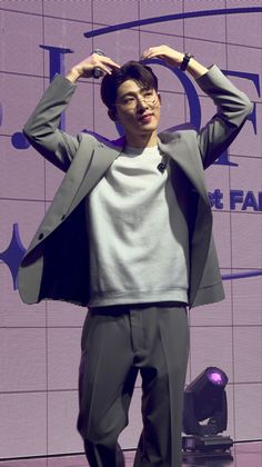 a young man is standing on stage with his hands behind his head and wearing glasses