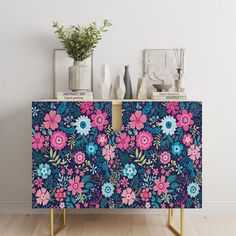 a blue and pink floral print cabinet with gold legs, vases and plants on top