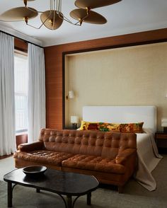 a living room with a couch, coffee table and lamps hanging from the ceiling in front of a large window