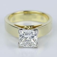 a gold ring with a princess cut diamond in the center, on a white background