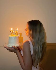 a woman holding a cake with candles in the shape of numbers on it, while wearing a white tank top