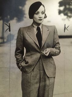 an old black and white photo of a woman in a suit standing with her hands on her hips