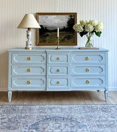 a blue dresser with flowers and a painting on the wall