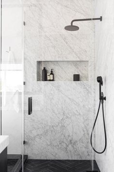 a bathroom with white marble walls and black flooring, shower head is on the wall