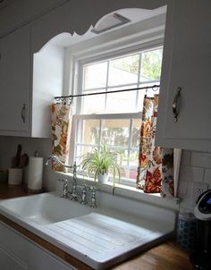 a white kitchen sink sitting under a window next to a counter top with a potted plant